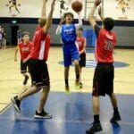 blue basketball player about to shoot and blocked by red players