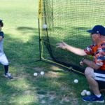 kid practicing batting a ball with a coach