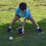 young boy catching a rolling ball with a mitt