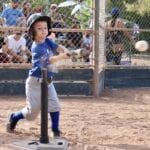 young kid in blue uniform hitting a tee ball