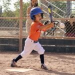 kid in orange uniform hitting a ball with a bat