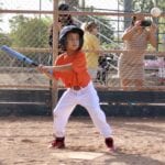 kid in orange uniform hitting a ball with a baseball bat