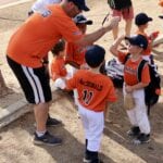 coach high fiving a kids in orange uniforms