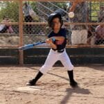 kid in dark blue uniform batting a ball
