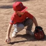 kid with red uniform picking up a baseball