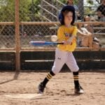 kid with yellow uniform about to hit a ball with a yellow bat
