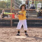 kid in yellow uniform swinging a baseball bat about to hit a ball