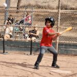 kid in orange uniform swinging a baseball bat