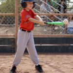 kid in orange uniform hitting a ball