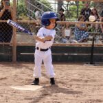 kid in white uniform swinging a bat