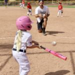 kid with pink helmet and bat hitting a ball
