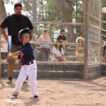 young boy in dark blue uniform raising a bat about to hit a baseball