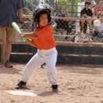 young boy in orange uniform about to hit a ball