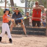 boy in orange uniform hitting a ball while an audience watches