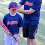 boy in blue uniform holding a bat with his coach