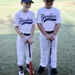 two boys in white uniforms and bats