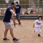 man pointing a base to a kid playing baseball