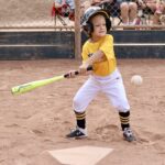 boy in yellow shirt about to hit a ball with a bat