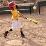 girl in yellow shirt about to hit a ball with a baseball bat