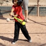 young boy in red shirt about to hit a ball with a baseball bat