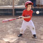 young boy in red shirt hitting a ball with a baseball bat