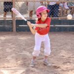 young girl in red shirt hitting a ball with a baseball bat