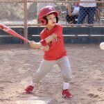 young boy in red shirt hitting a baseball ball with a bat