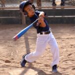 boy in blue shirt about to hit a ball with a bat