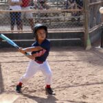 boy in uniform shirt swinging a bat