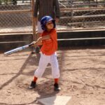boy in orange shirt about to hit a ball with a bat