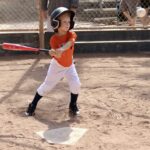 boy in orange shirt swinging a bat