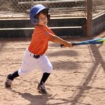 kid in orange shirt swinging a bat