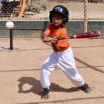 boy in orange shirt about to hit a ball with a baseball bat