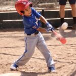 young boy in blue shirt about to hit a ball with a bat