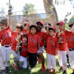 group of kids with red shirts raising their trophies